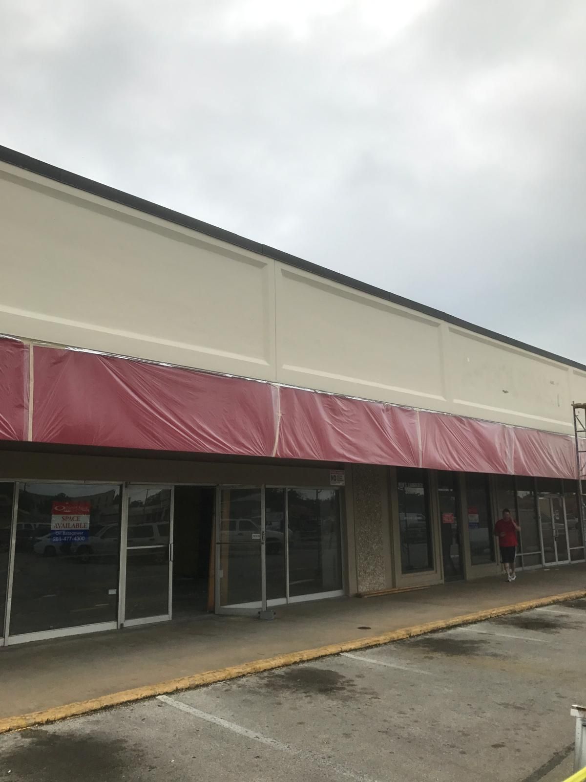 Storefront with red awning. Cloudy sky. Parking lot. A person walks on the sidewalk.