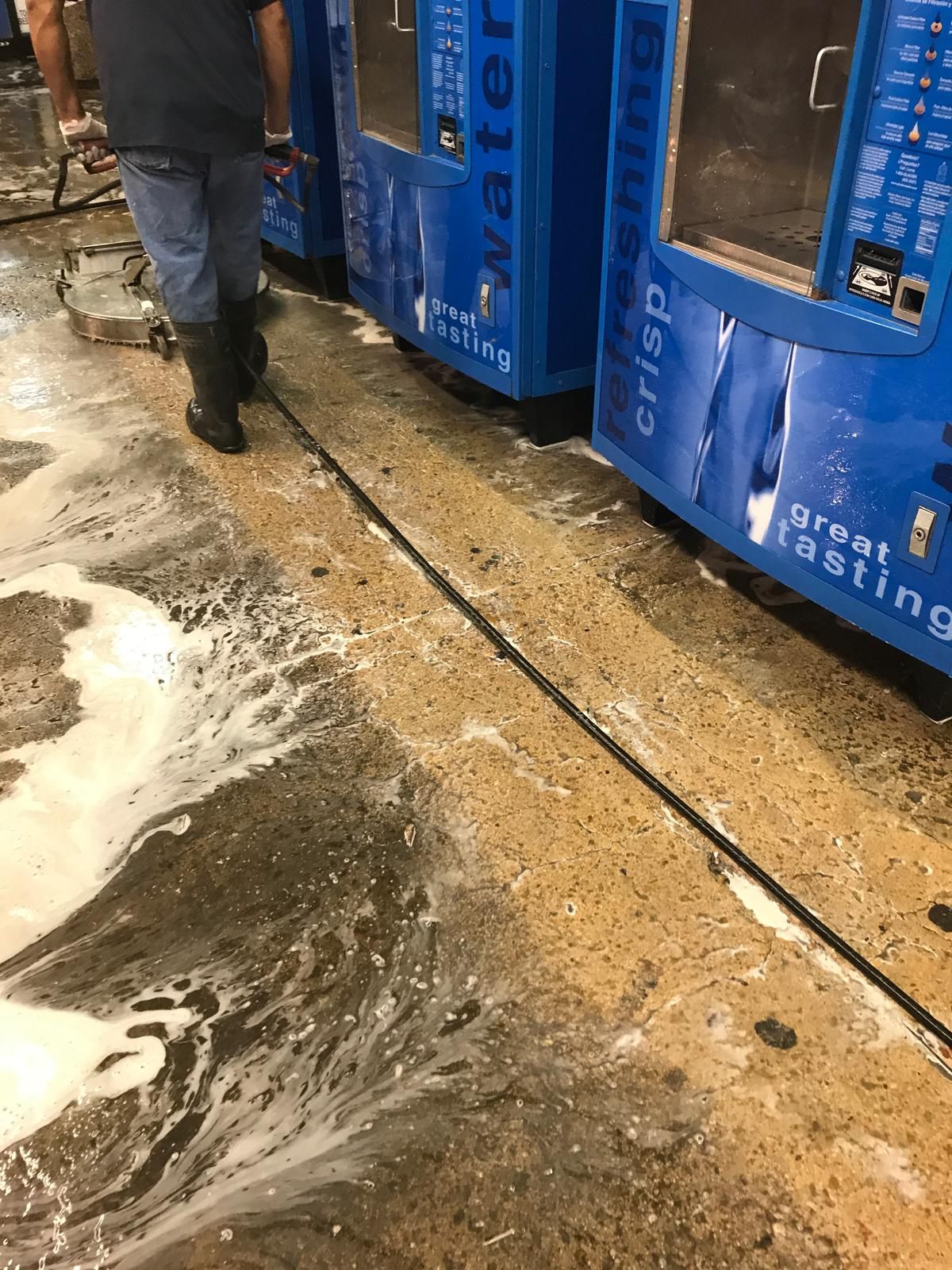 Person walks on wet concrete next to blue water vending machines, cleaning area.