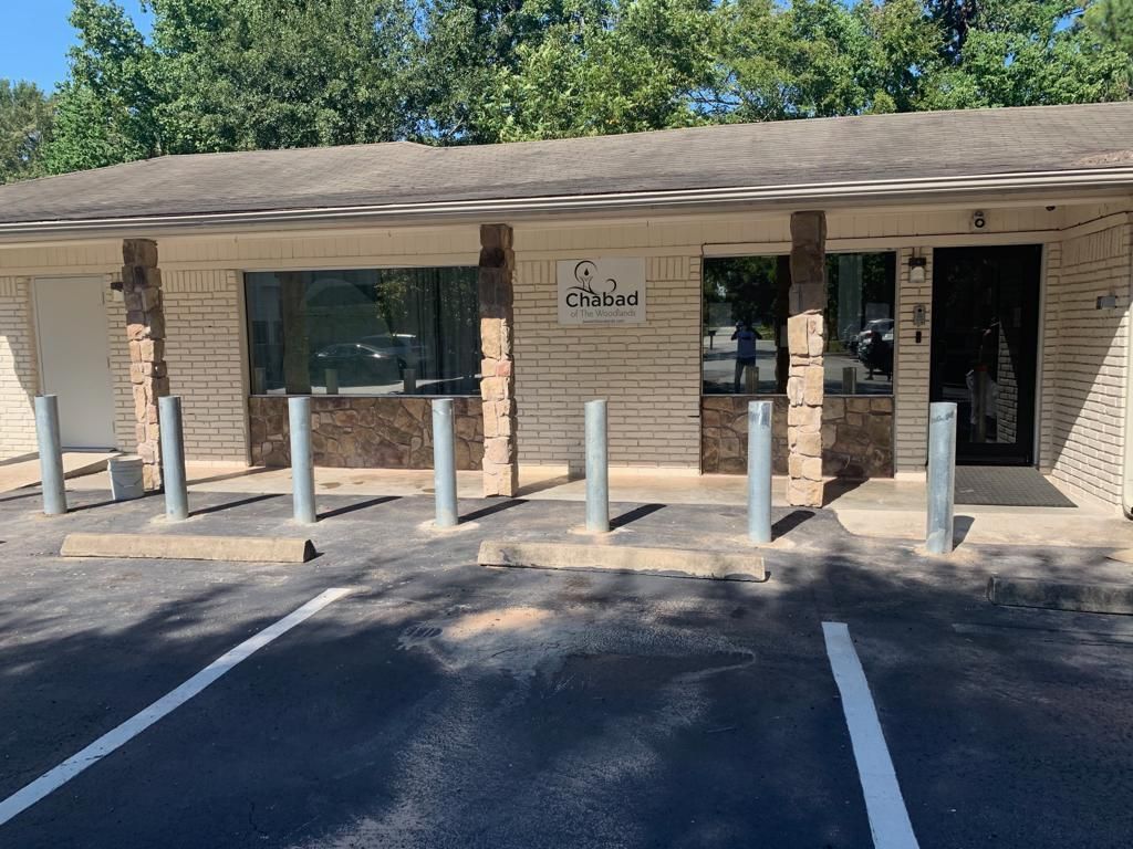 Exterior of a low, tan brick building with a dark roof and columns. Parking spots are marked in the foreground.