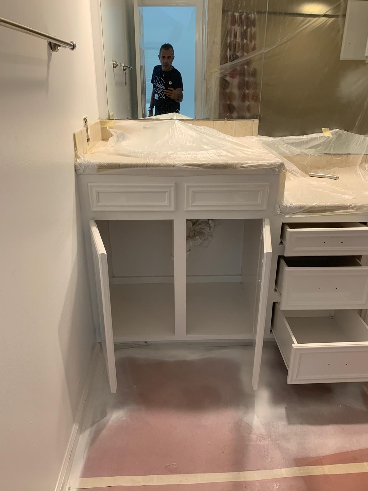 White bathroom vanity with open doors, a person in the mirror.