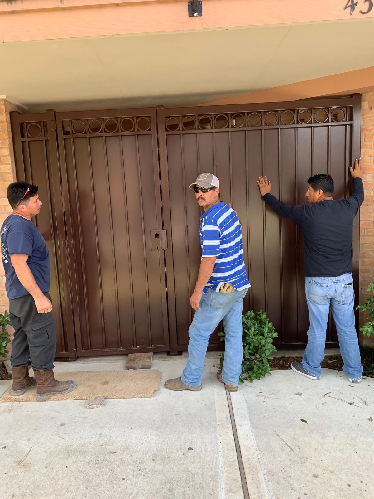 Three men installing a brown metal gate at a house; one is smiling.