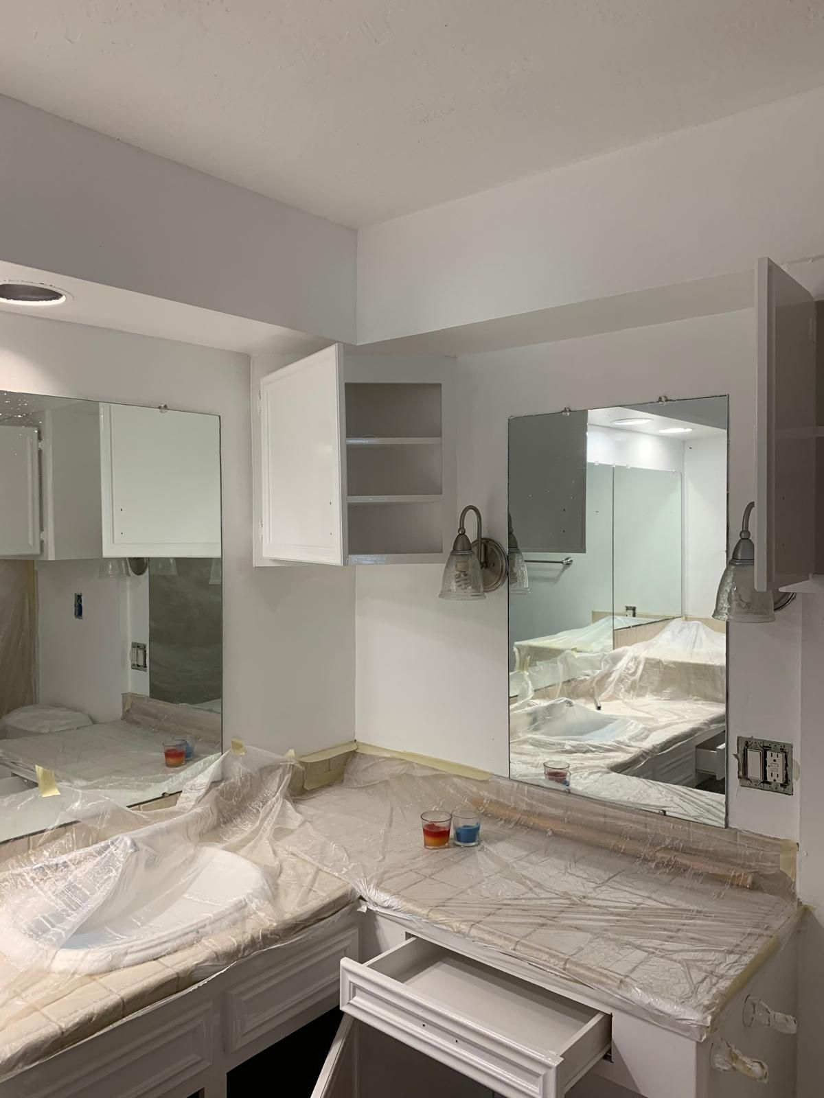 Bathroom under renovation with white cabinets, marble countertop, and open drawer.