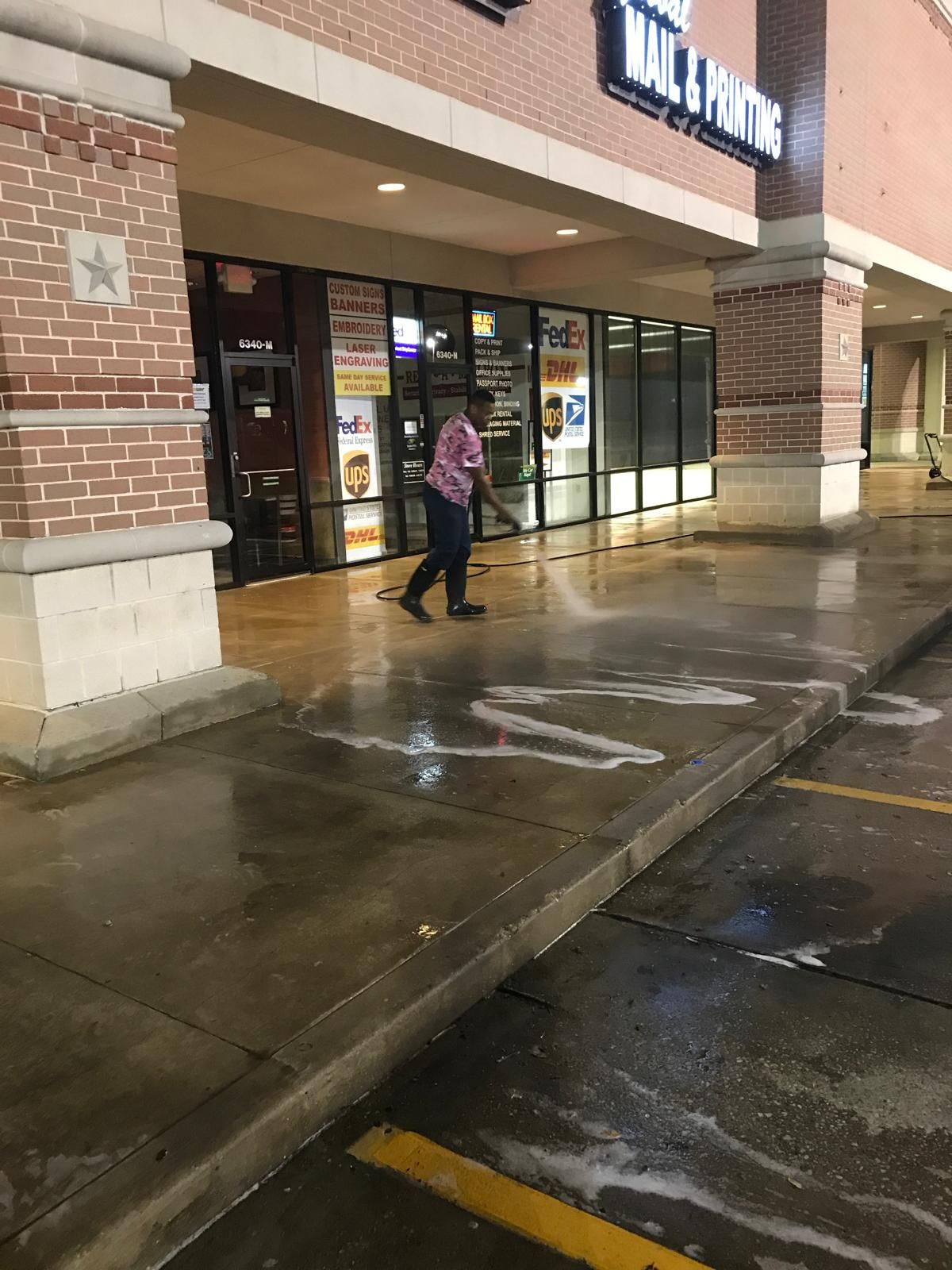 Person power washing the sidewalk in front of a shopping center.