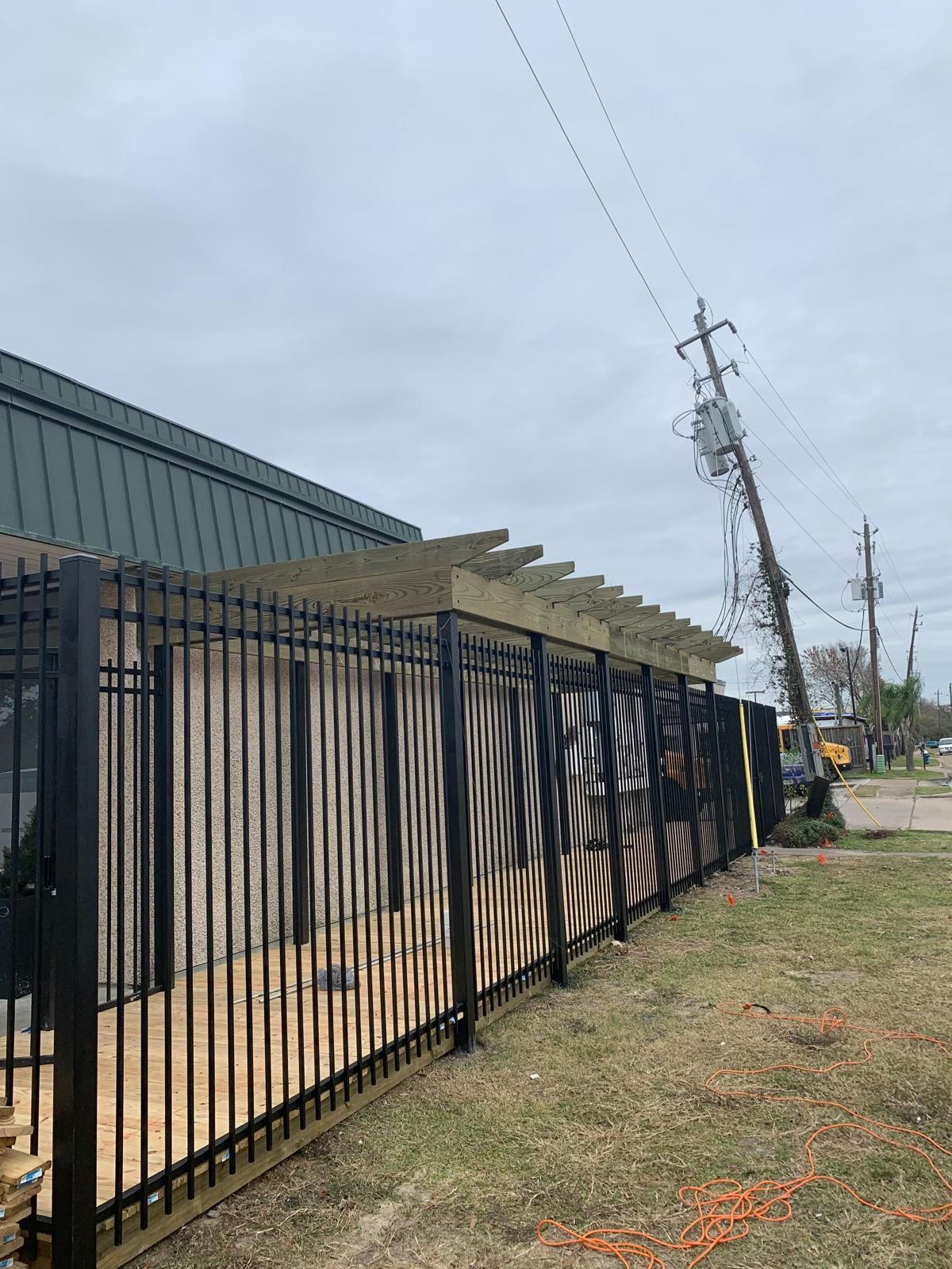 Black metal fence with wooden structure extending from the building. Power lines and utility pole in the background.