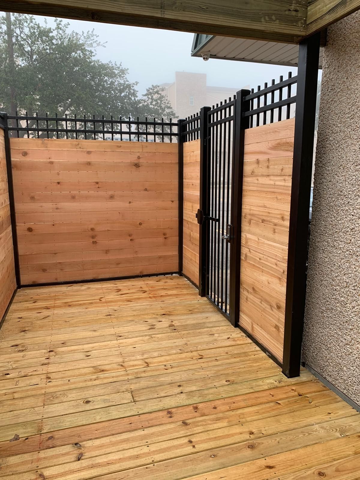 Wooden deck enclosed by horizontal wood panels and a black metal fence and gate.