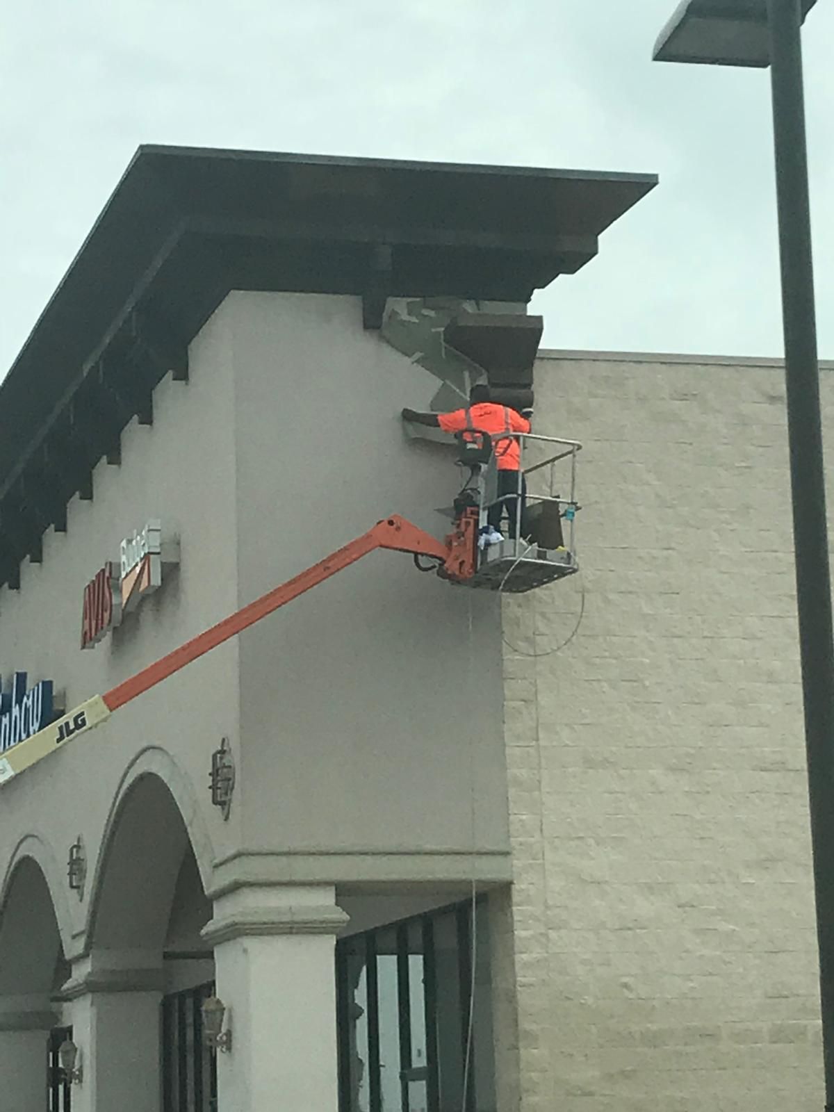 Person in orange vest on lift repairing building facade.