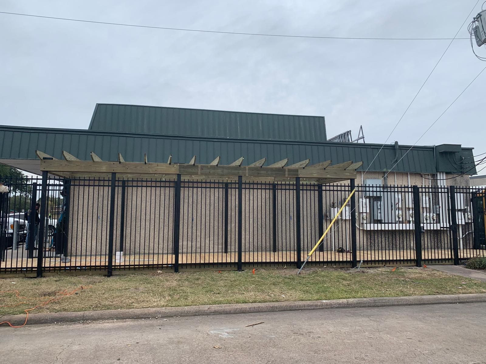 Building with a fence; green roof, bamboo facade, black metal fence, overcast sky.
