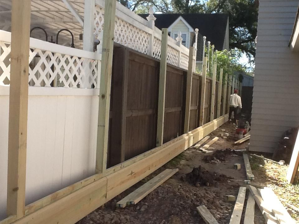 Fence construction in progress: wood posts and boards next to existing white and brown fence sections; person in background.