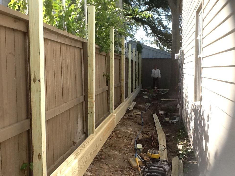 Fence under construction: wooden posts and boards alongside an existing fence. A person stands in the distance.