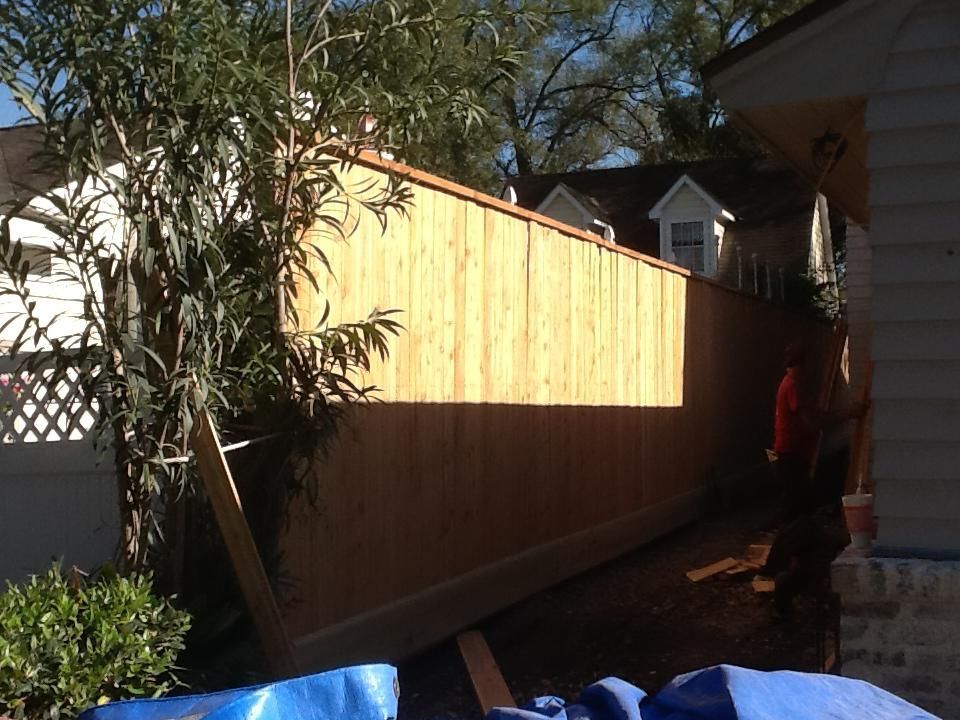 Wooden fence being built next to a house with blue tarps and greenery around.