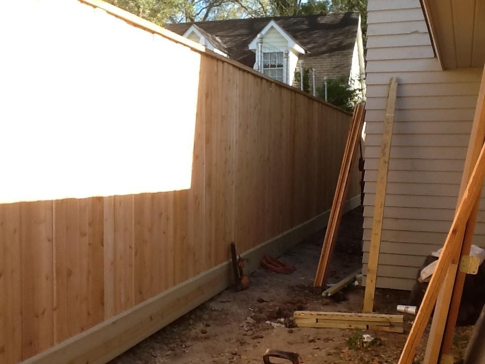 New wooden fence next to a house, under construction; cedar color.