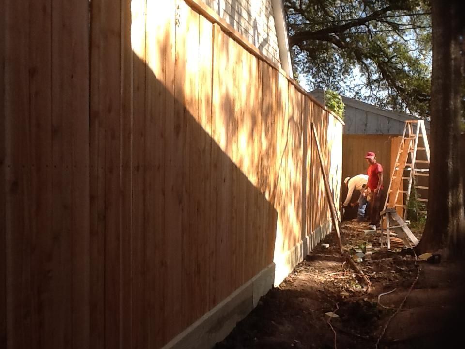 Wooden fence being built; two workers by the fence, one wearing red.
