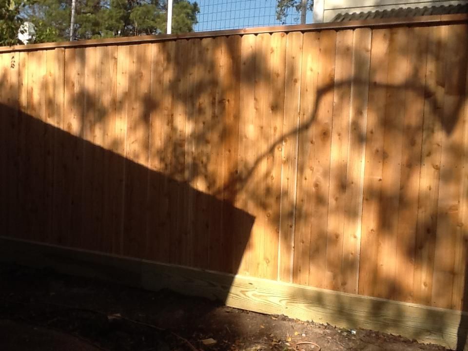 Wooden fence with shadows of a tree cast upon it. The fence is bathed in sunlight.