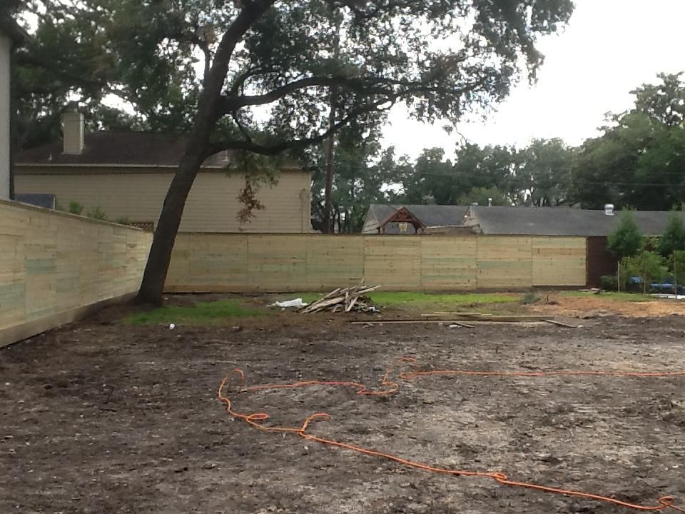 Brown yard with a wooden fence and a tree. Orange cable laid out on the ground.
