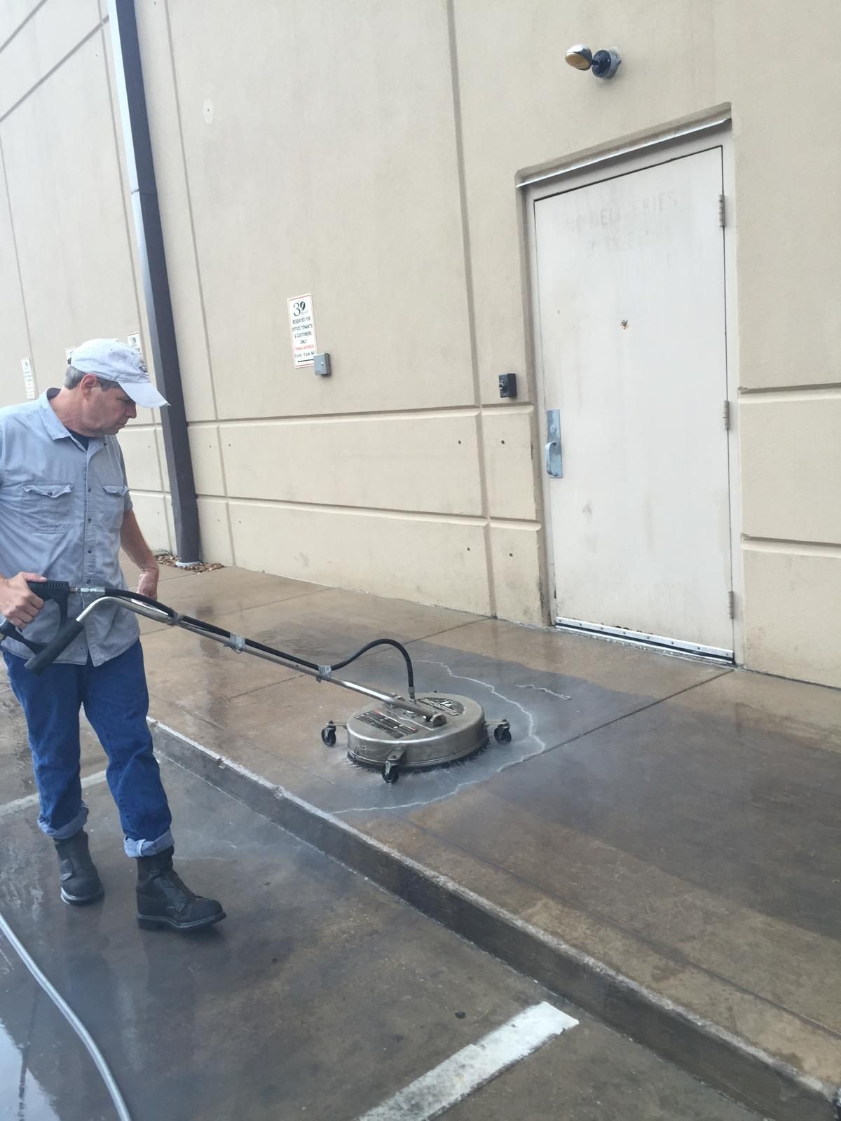 Man power washing a concrete walkway outside a building; white and gray colors.