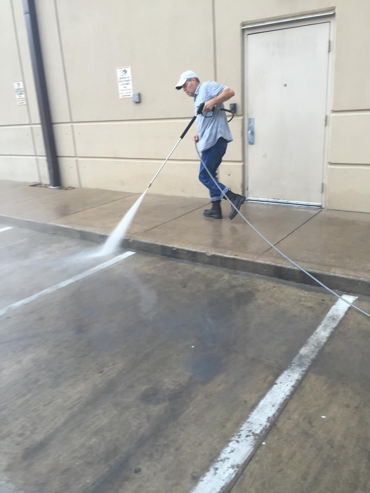 Man pressure washing a concrete surface outside a building.