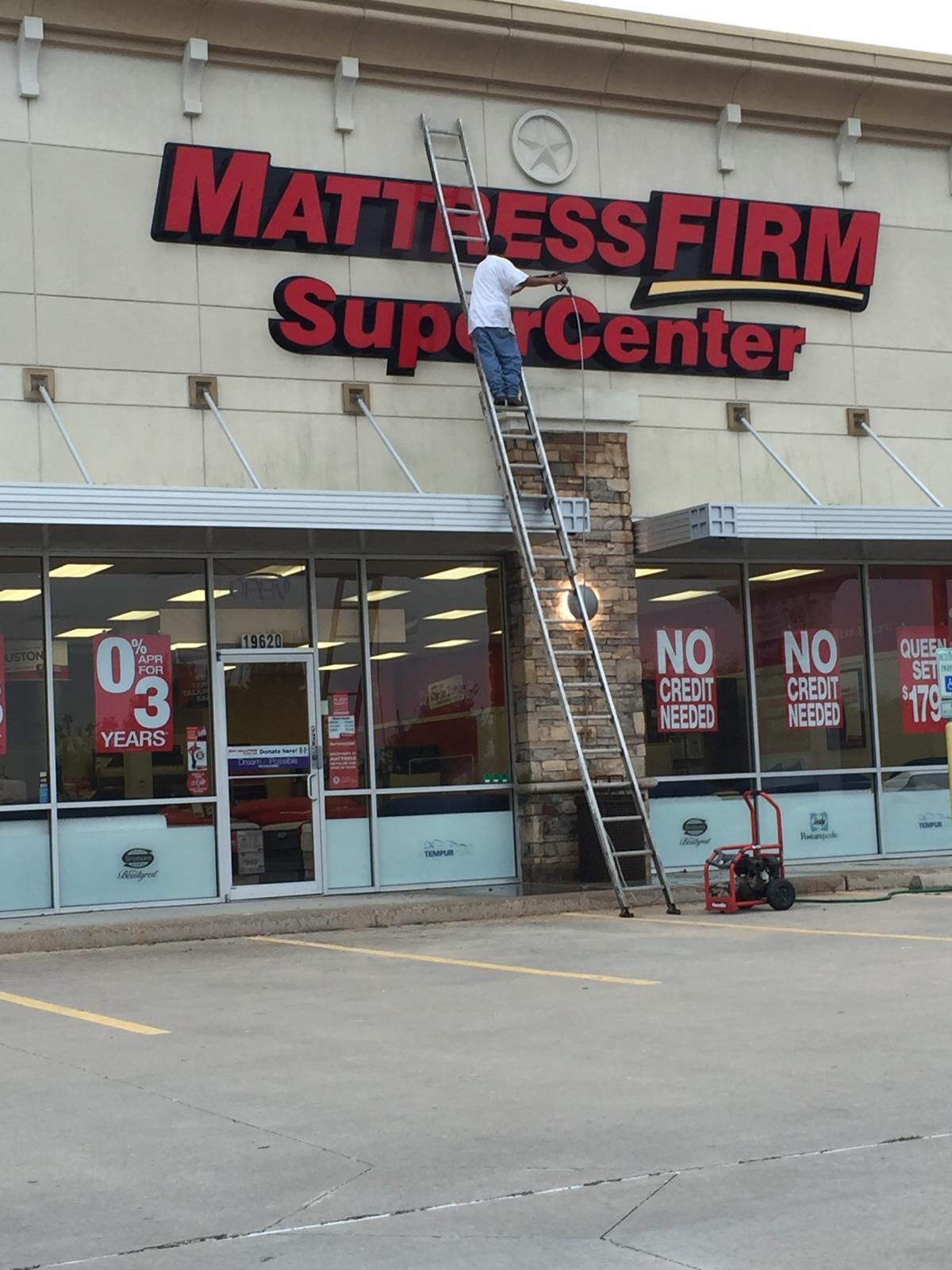 Man on a ladder working on a Mattress Firm sign at a SuperCenter; red letters, store exterior.