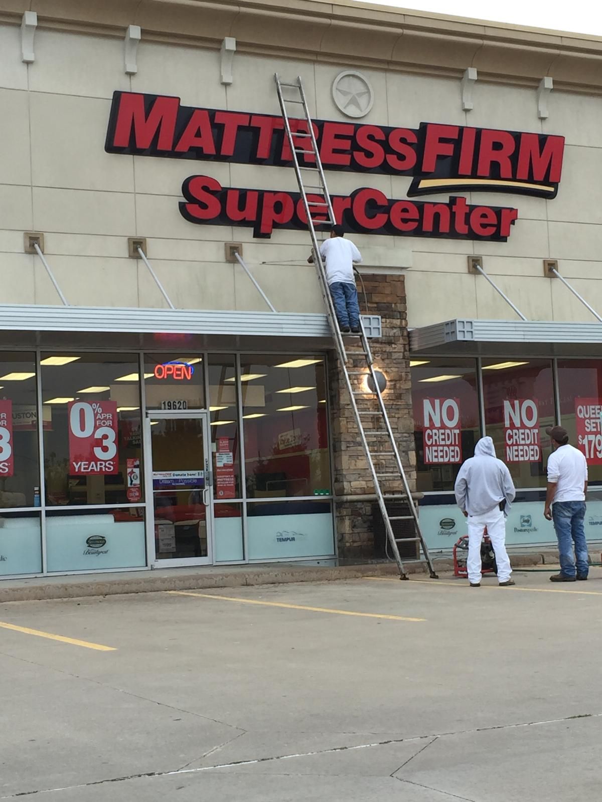 Man on a ladder repairing a Mattress Firm sign. Two men watch below.