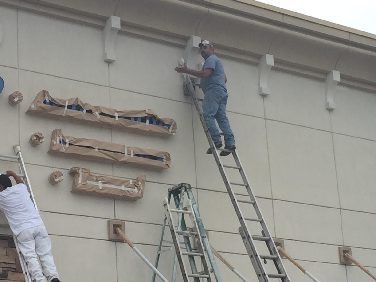 Workers on ladders installing signage on a beige building.