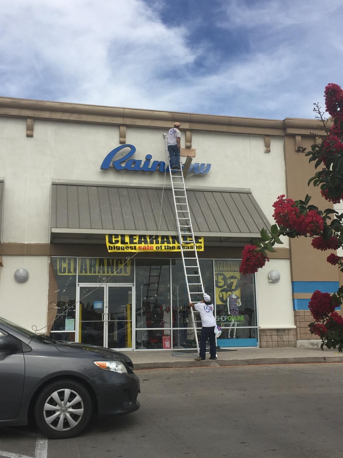 Two men on a tall ladder working on a store sign that says 