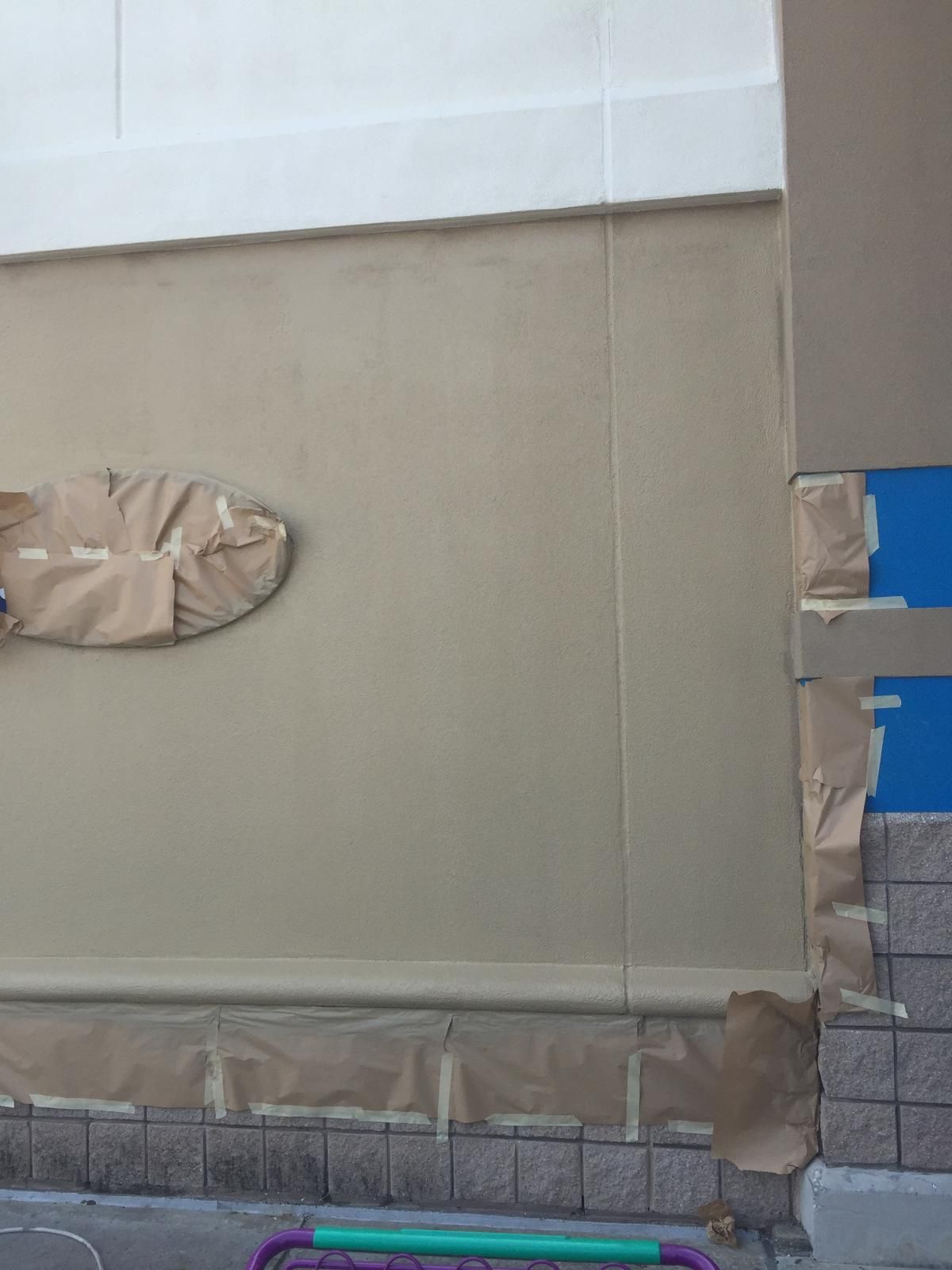 Exterior wall being painted beige with white trim, taped off areas.