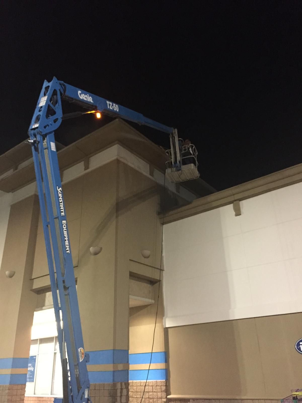 A blue Genie lift extended to the top of a building, worker in the bucket, nighttime.