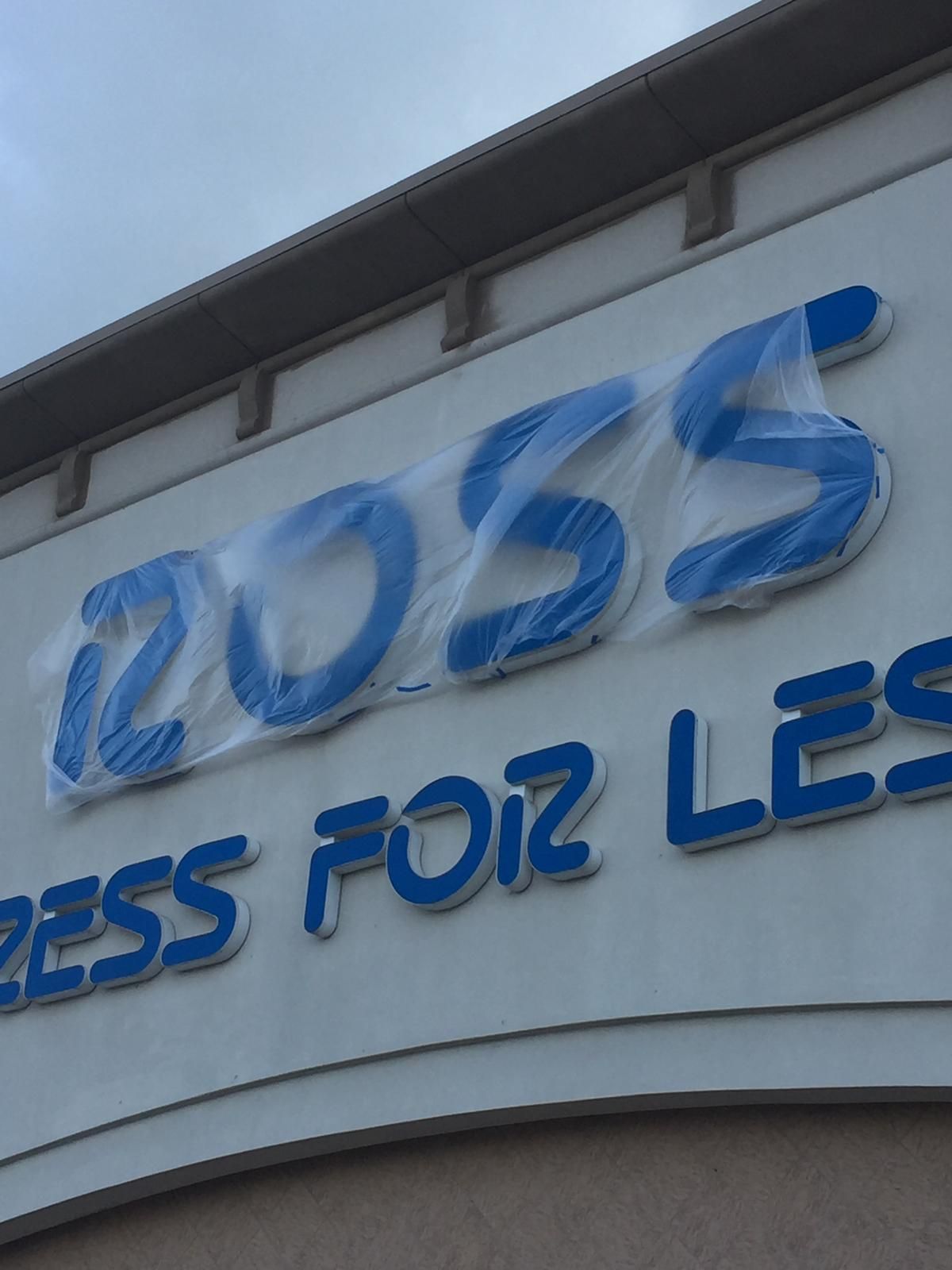 Signage for Ross Dress for Less, with blue letters partially covered in clear plastic, on a building exterior.