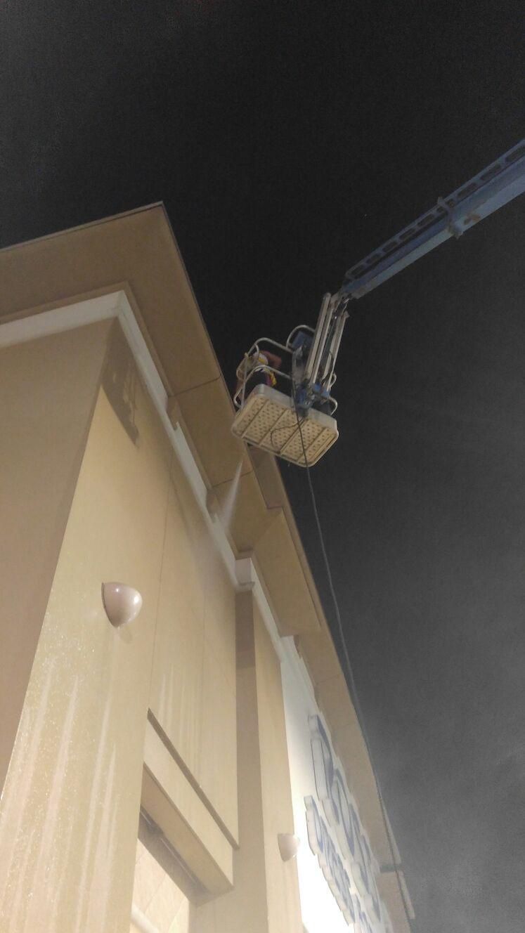 A cherry picker with worker near a building's trim at night, possibly doing repairs.