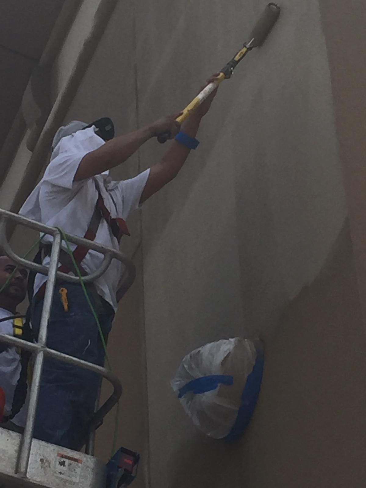 Man on lift painting exterior wall with extension pole.
