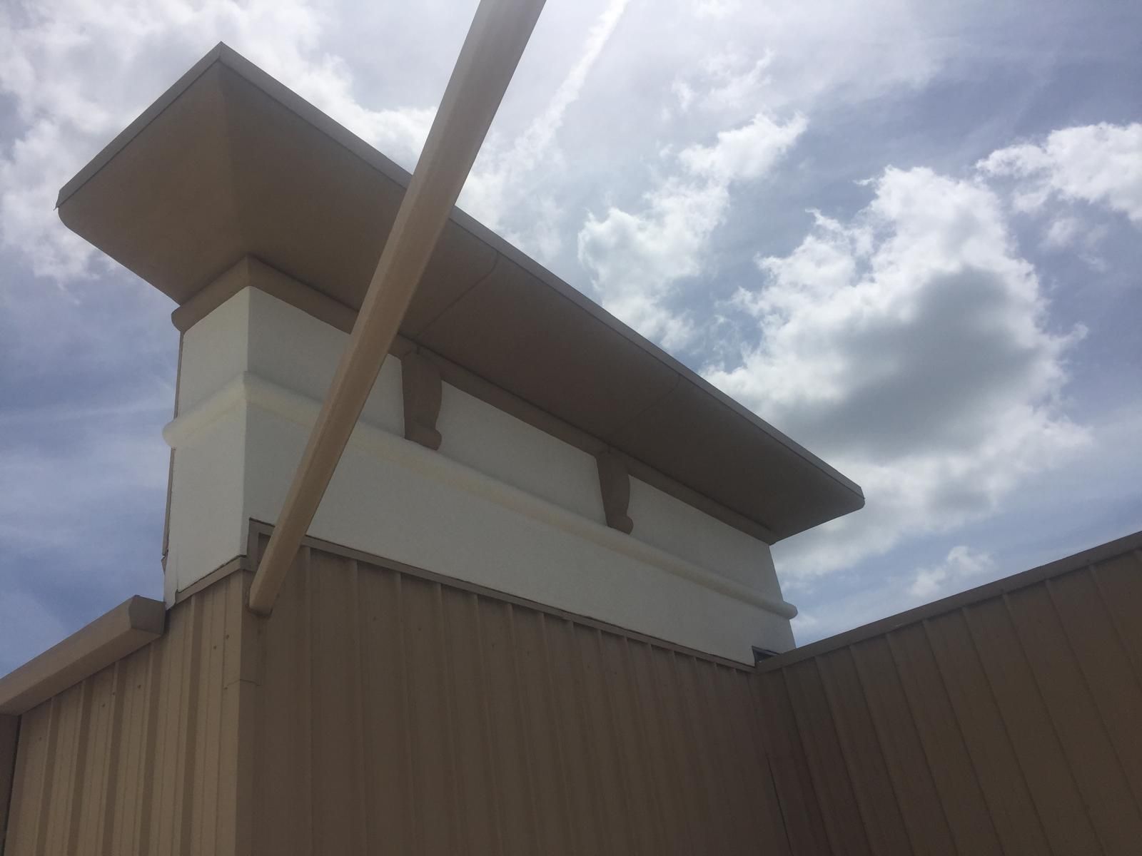 Tan and white building rooftop with a box-like structure on top under a partly cloudy sky.
