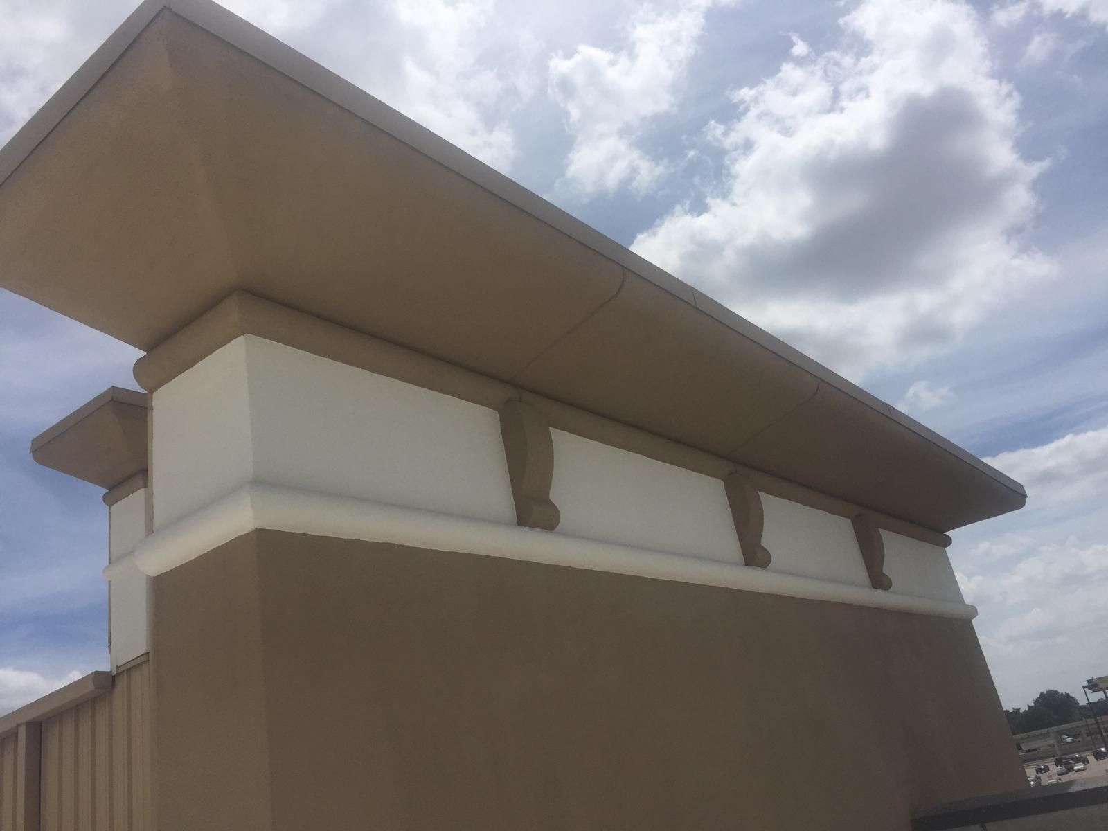 Tan and white building exterior with a flat roof against a cloudy sky.