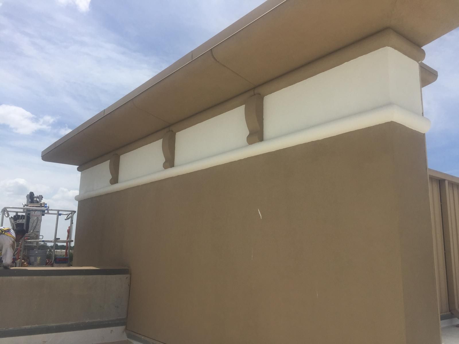 Tan and white painted rooftop wall with rectangular accents under a cloudy sky.
