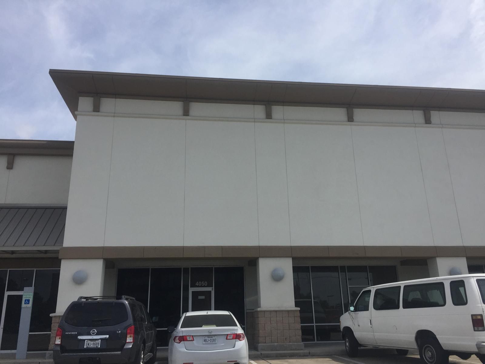 Exterior of a beige commercial building with a flat roof, windows, and parked vehicles.