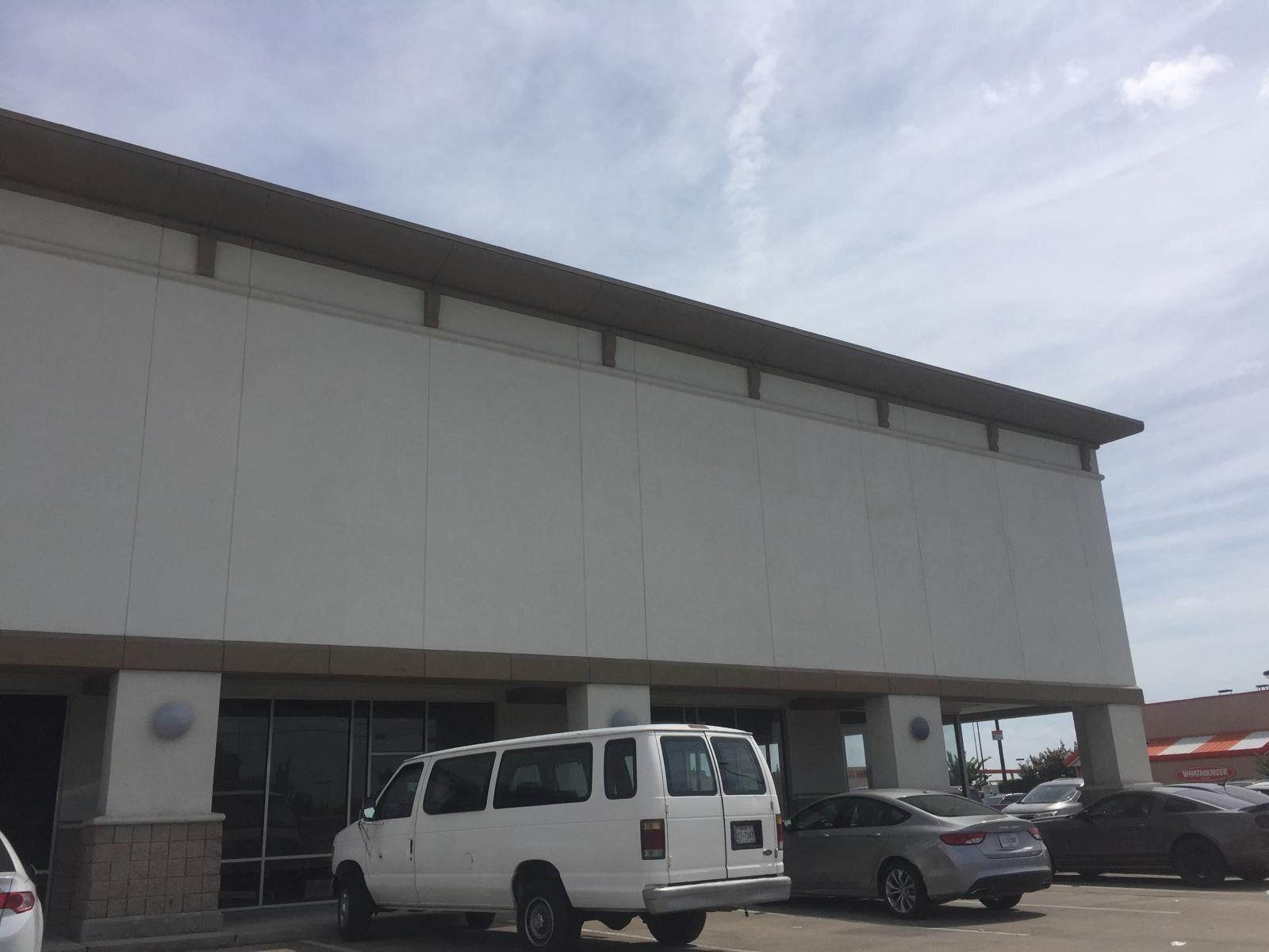 White van parked in front of a plain white building with brown trim and windows. Cloudy sky.