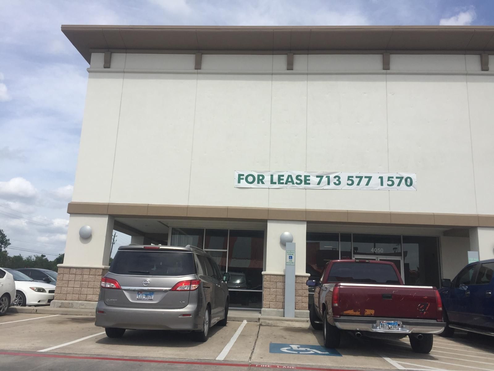 Building for lease; gray minivan, red truck parked in front; sign: 