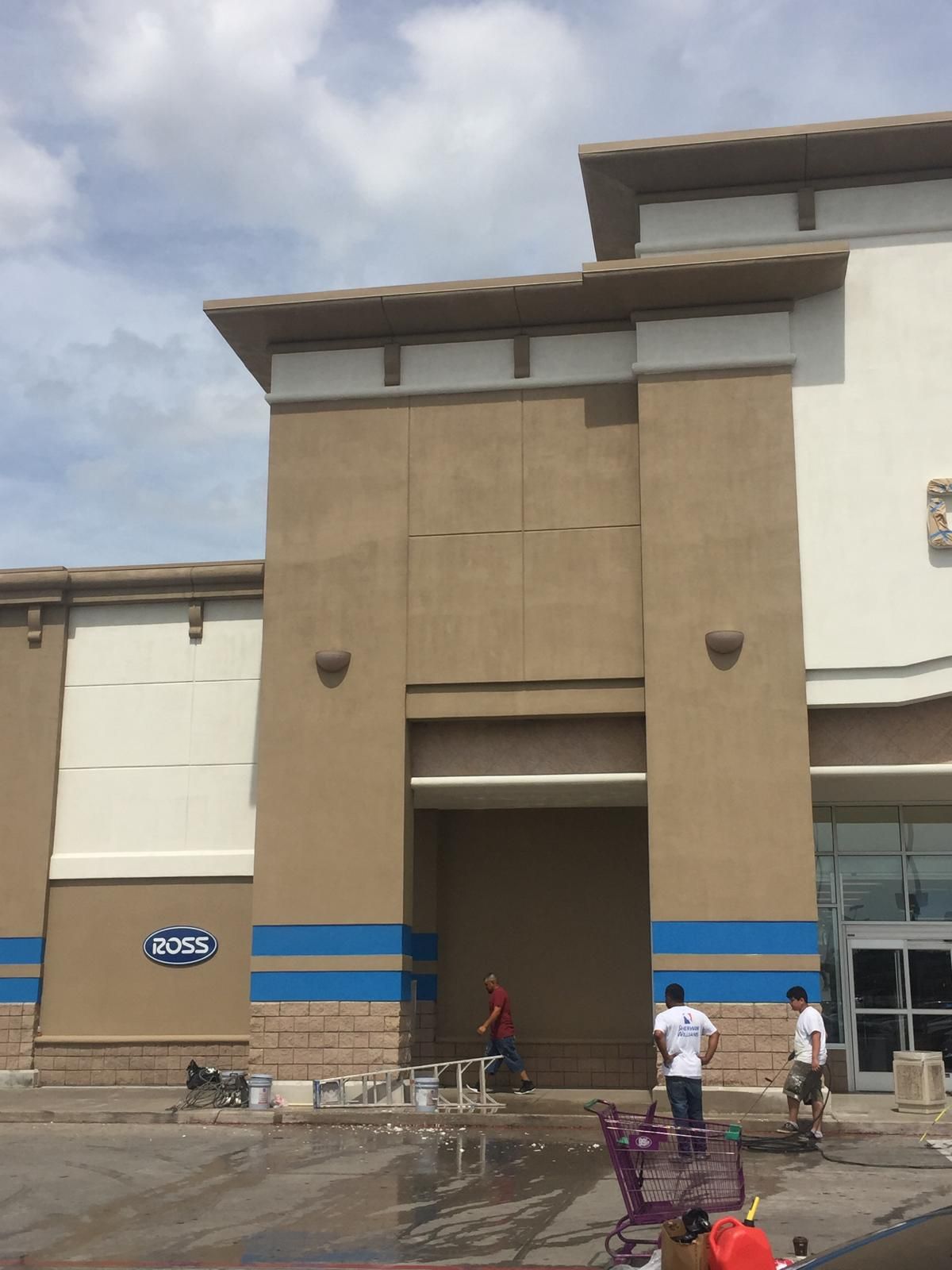 Exterior of a store being painted; workers, beige/white building, blue stripes, overcast sky.