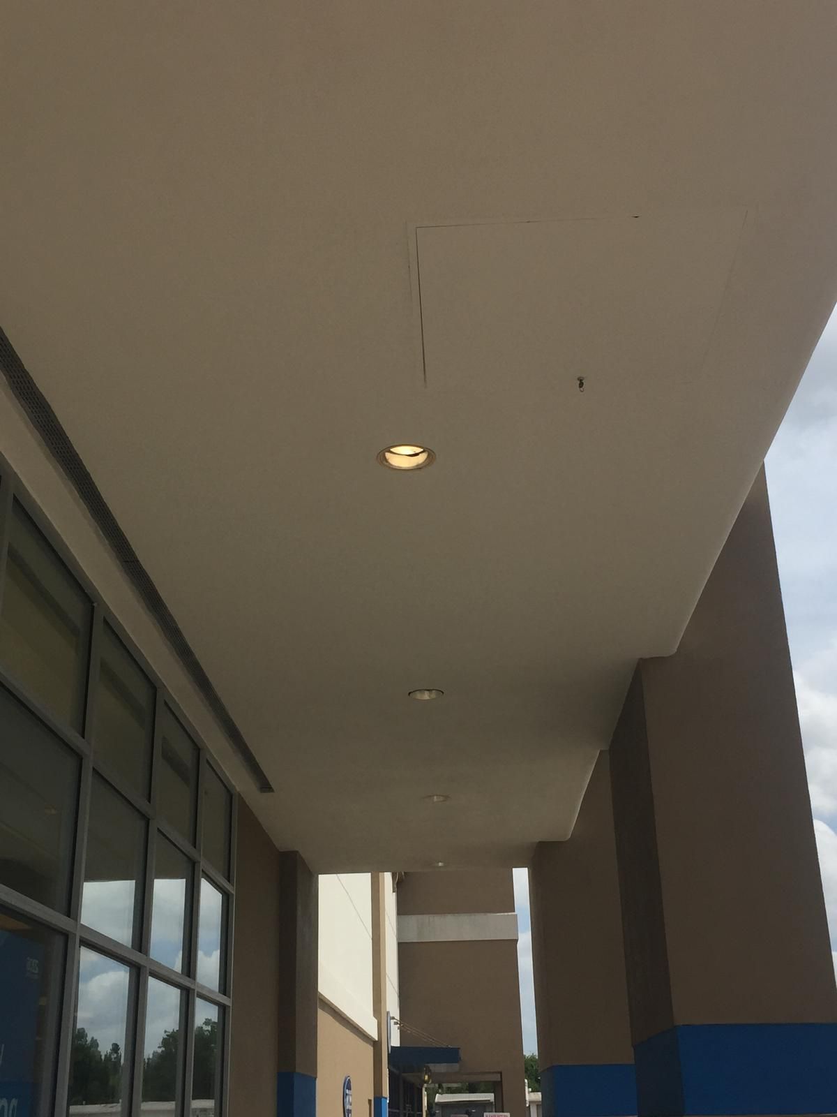 Exterior view of a building's covered walkway, with ceiling lights and columns; tan and blue accents.
