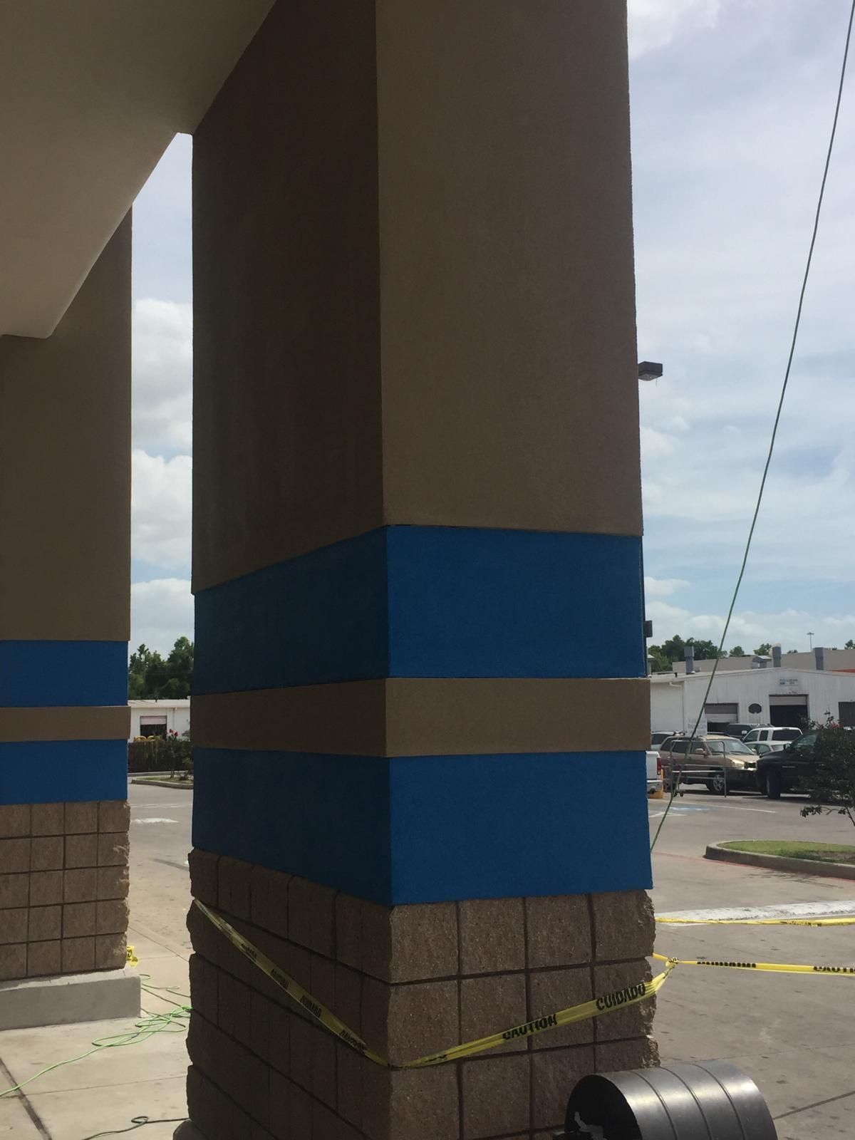 Column of tan and blue painted building, lower portion with a brick pattern, yellow caution tape.