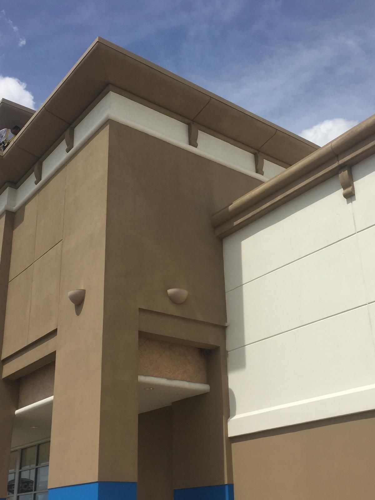 Tan and white building exterior with a blue base against a cloudy sky.