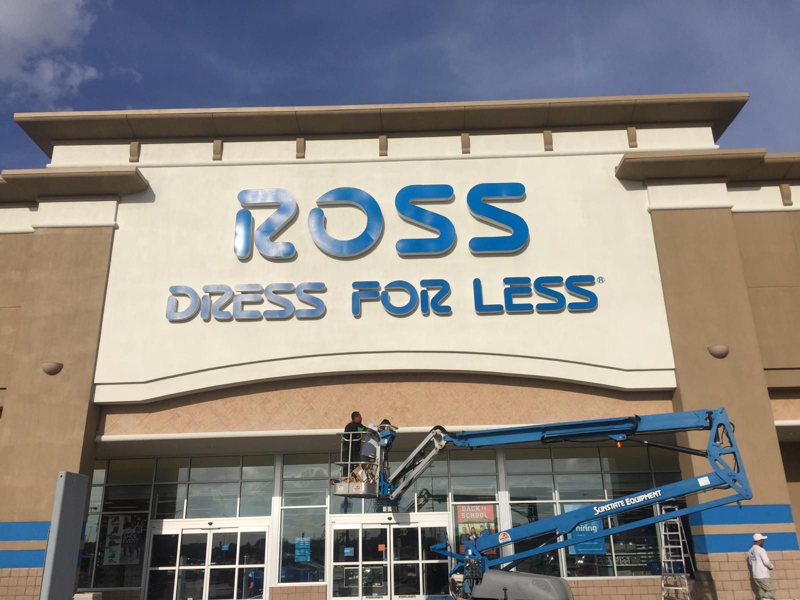 Ross Dress for Less store front with workers in a lift, blue signage, and a partly cloudy sky.