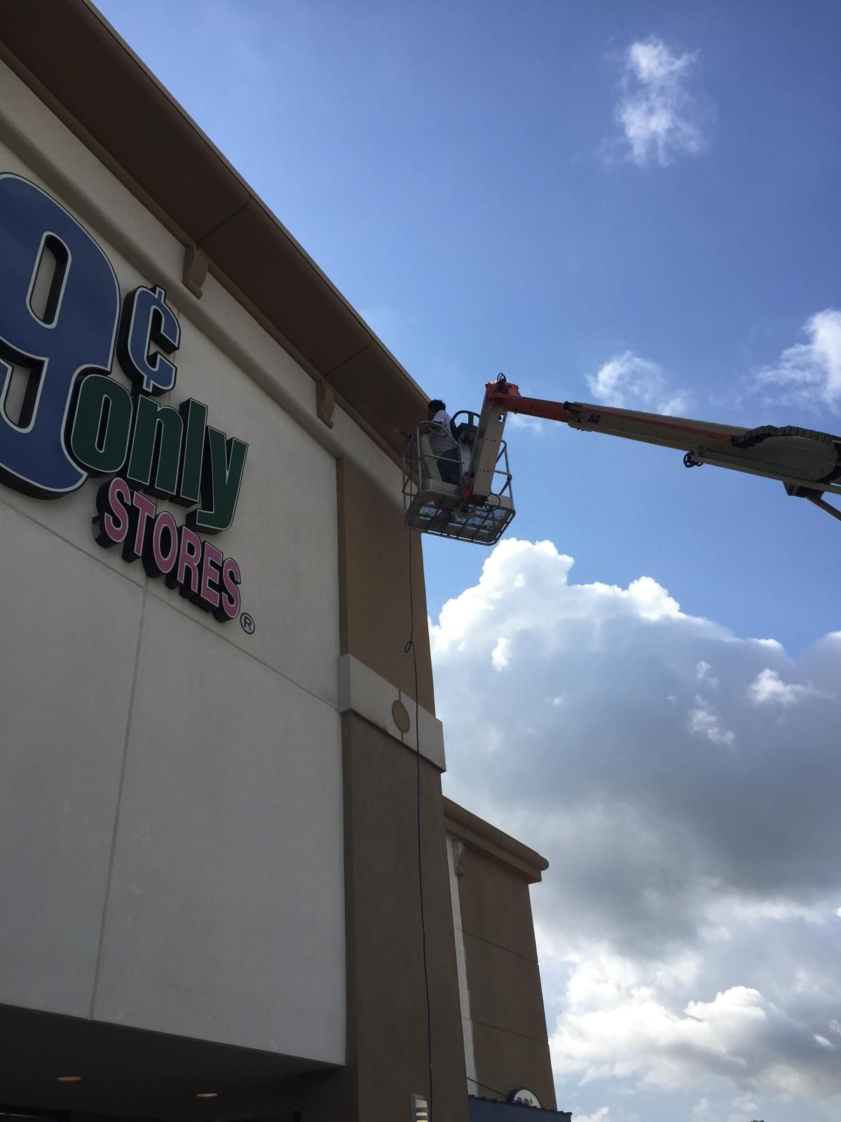 A worker in a lift bucket repairs the sign of a 99 Cents Only Stores building.