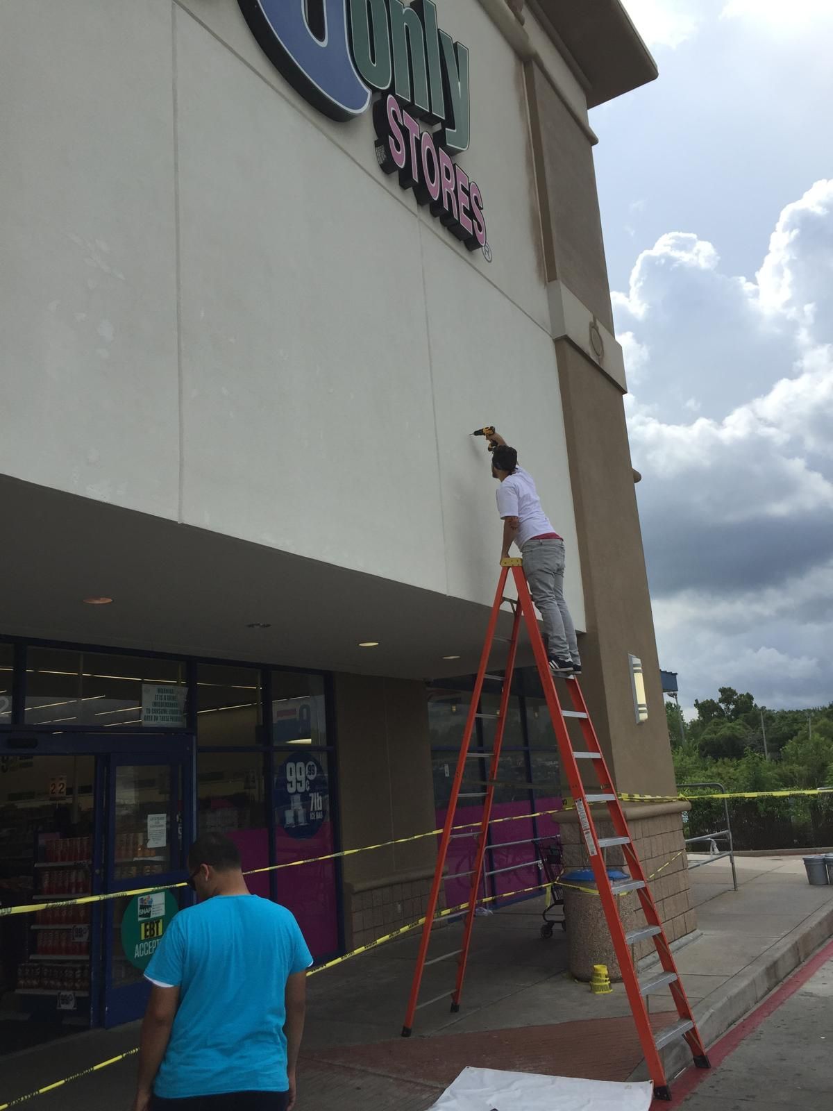 Person on a ladder painting a wall above the entrance to a Dollar Store.