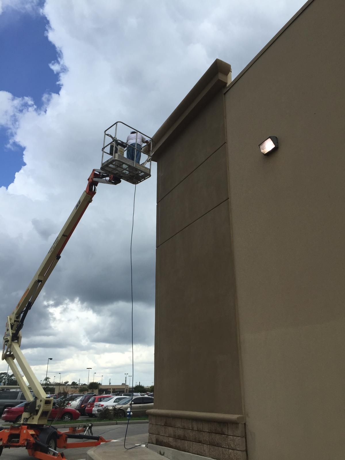 Person in lift painting building's exterior under a cloudy sky.
