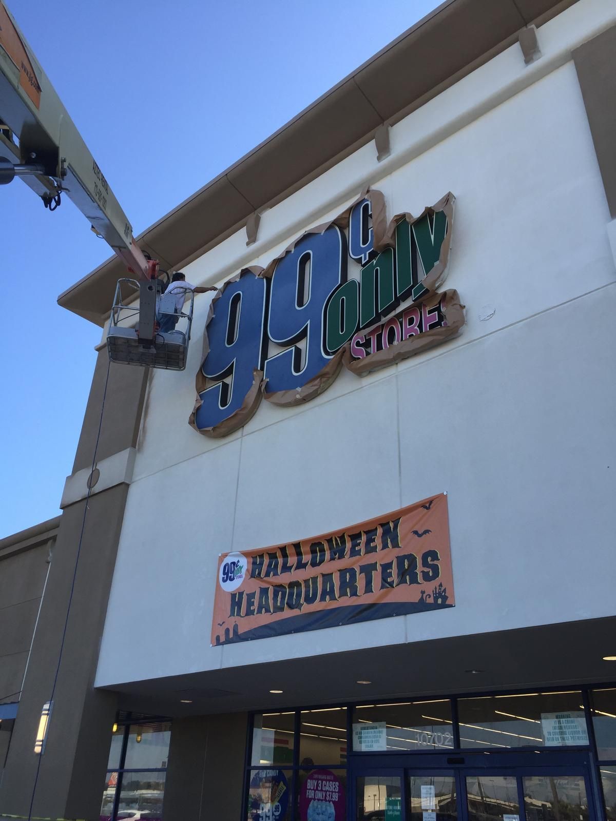 Person on lift working on the 99 Cents Only Stores sign. Halloween Headquarters banner below.