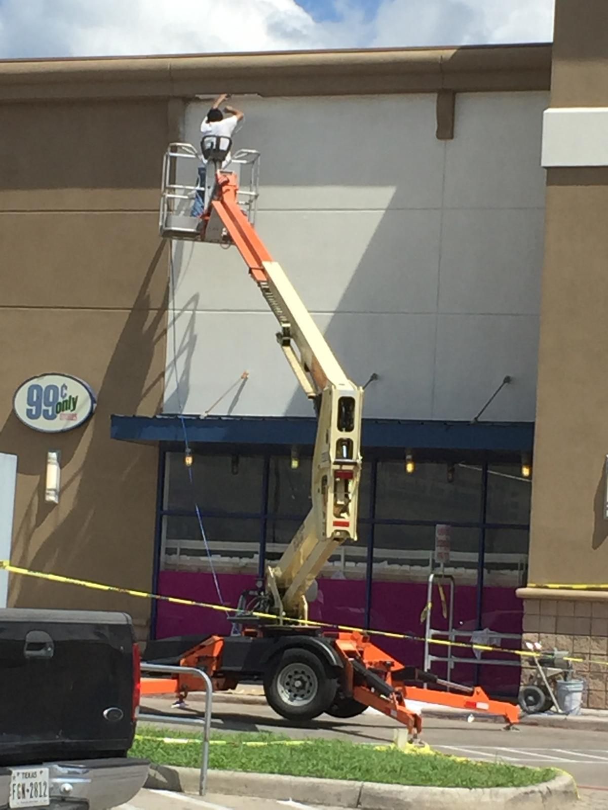 A person in a lift working on a building's exterior above a 99 Cents Only store.