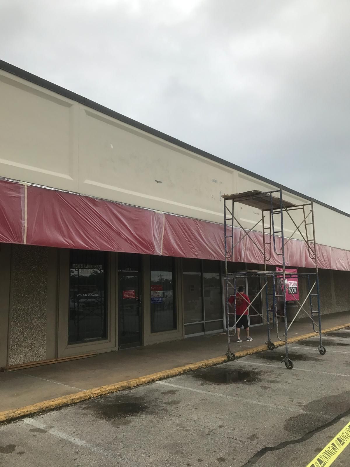 Scaffolding set up in front of a commercial building's red awning, possibly for exterior work.