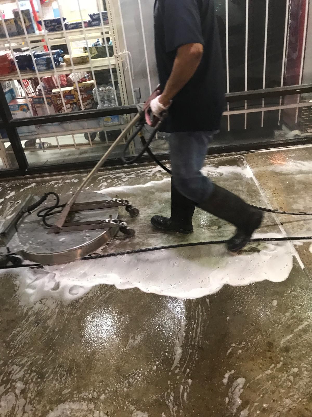 Person pressure washing a concrete surface with foam in front of a store.