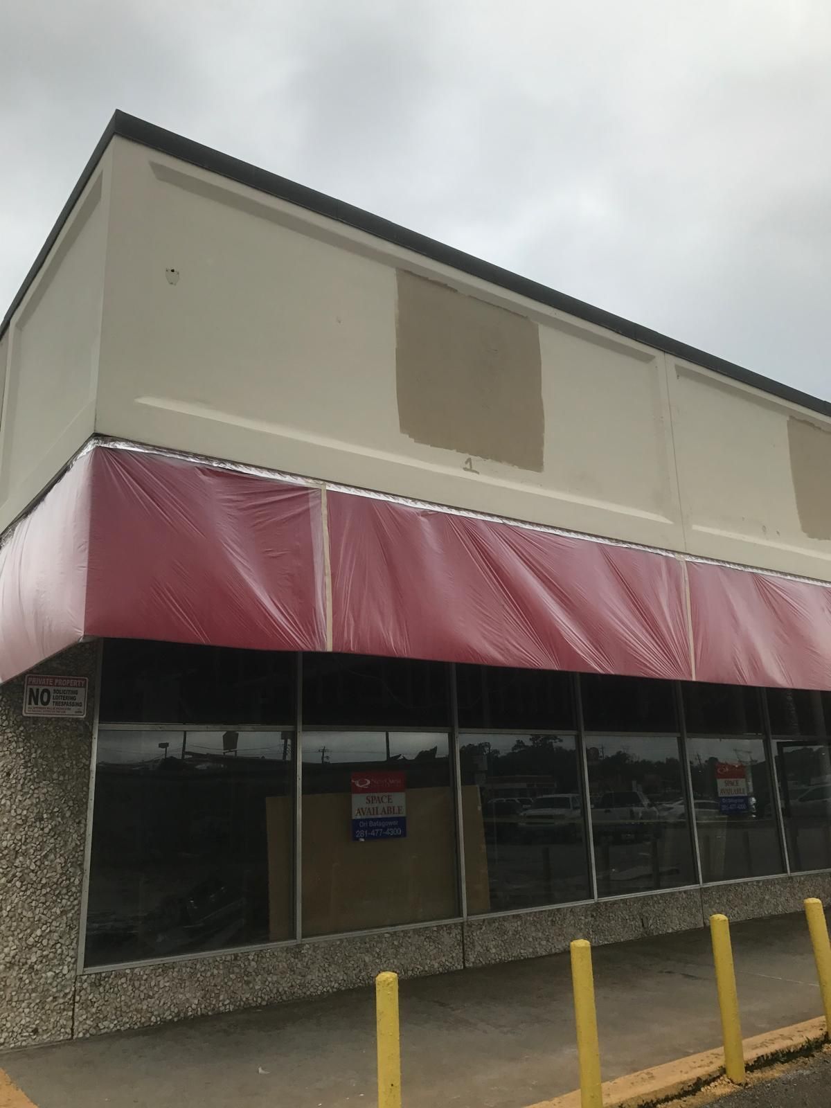Exterior of a vacant commercial building with a red awning, concrete facade, and reflective glass windows.
