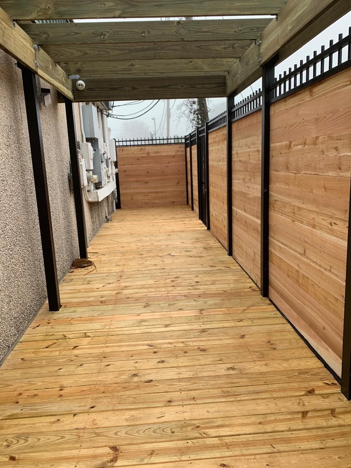 Wooden walkway with a wood-planked deck and wooden fence. A security camera is attached to a wooden beam.