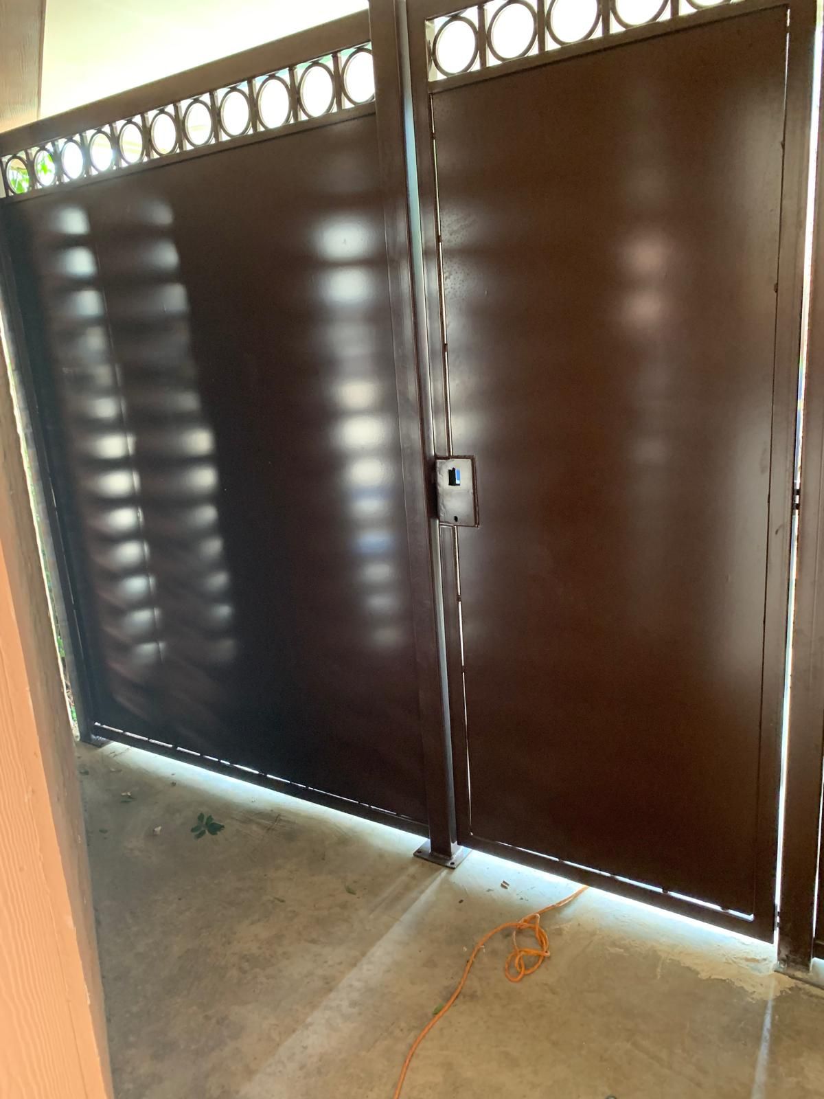 Brown metal gate with a decorative top, a lock, and sunlight shadows.